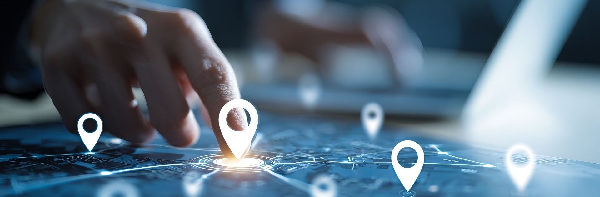La main d'une personne touchant une tablette affichant une carte numérique avec de multiples points de localisation. L'image représente l'utilisation d'un logiciel de gestion de flotte pour la géolocalisation, le geofencing et la surveillance GPS en temps réel des actifs ou véhicules.